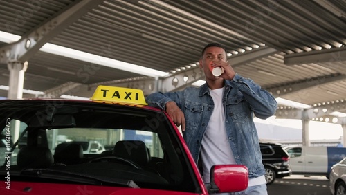 Happy taxi driver drinking coffee, leaning on the red car.