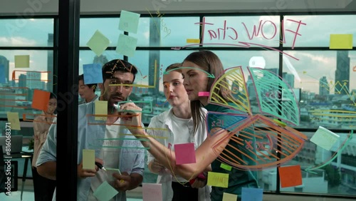 Smart business team working together to brainstorm marketing plan while putting sticky notes on glass wall with statistic graph. Group of businesspeople sharing, thinking,discussing idea. Tracery