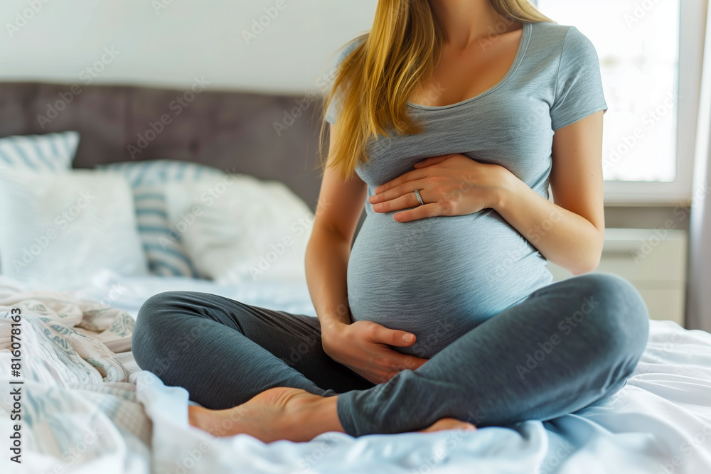 Pregnant woman with visible belly sitting on bed