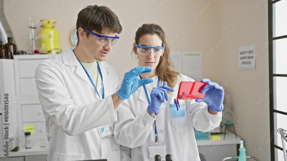 Two scientists, a man and woman, analyze data on a mobile phone in a laboratory setting. Two scientists, a man and woman, analyze data on a mobile phone in a laboratory setting.