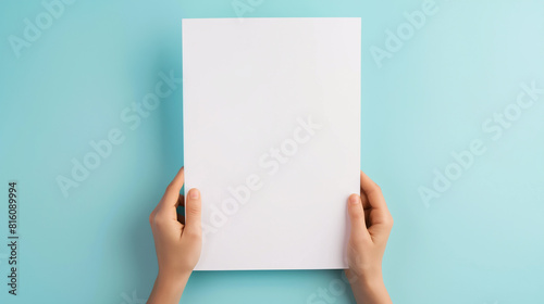 Mãos femininas segurando uma folha de papel branco em branco sobre fundo azul claro. Vista do topo. Papel de maquete com espaço de cópia para texto