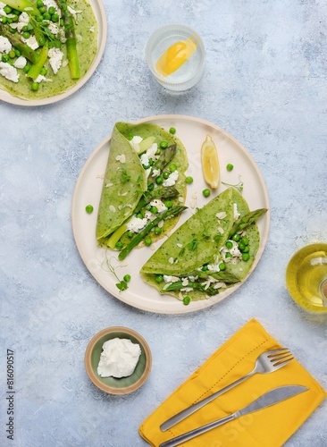 Green pancakes with spinach and nettles, stuffed with asparagus, green peas and ricotta on a ceramic plate on a gray concrete background. Seasonal products, recipes. Asparagus recipes.