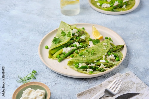 Green pancakes with spinach and nettles, stuffed with asparagus, green peas and ricotta on a ceramic plate on a gray concrete background. Seasonal products, recipes. Asparagus recipes.