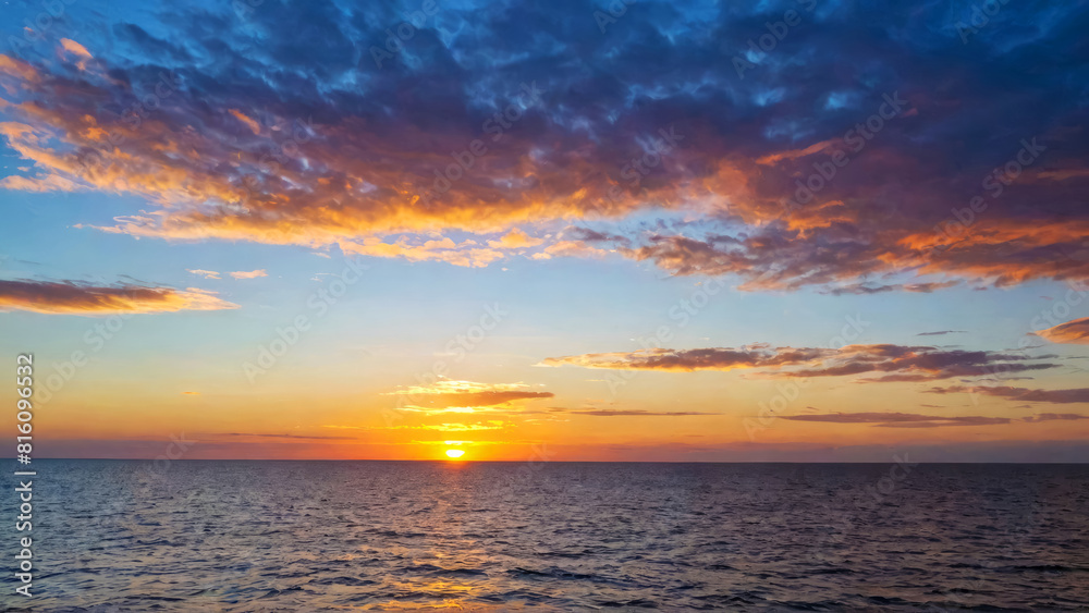 Sunset casts warm red glow over calm sea, with light breeze gently rippling surface. Fluffy clouds drift across sky, edges illuminated by setting sun's radiant light. Serene, tranquil atmosphere. Sunset casts warm red glow over calm sea, with light breeze gently rippling surface. Fluffy clouds drift across sky, edges illuminated by setting sun's radiant light. Serene, tranquil atmosphere.