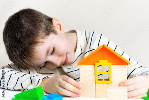 Cute boy build a house of wooden cubes and blocks constructor. Playing toddler,child plays at home. Parenting, safety, insurance, credit, real estate and mortgage financial concept.