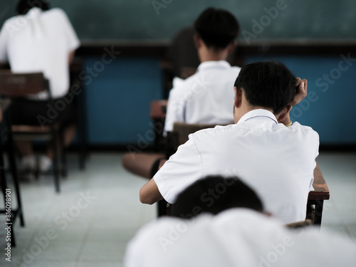 Students reading exam answer sheets exercises in classroom of school with headache.and stress