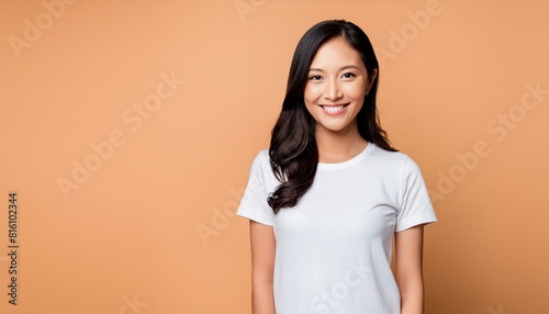 Portrait of a smilling asian woman wearing a white t-shirt and jeans,isolated on solid peach color background
