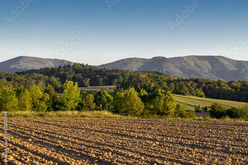 Landscape with trees, mountains and a plowed field in the light of the golden hour 