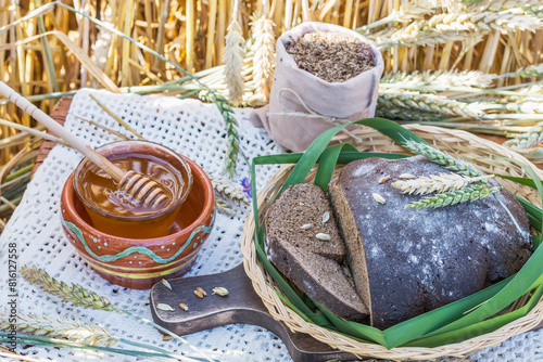 Sliced rye bread, fresh honey and bag of cumin on lace tablecloth with wheat ears in wheat field background