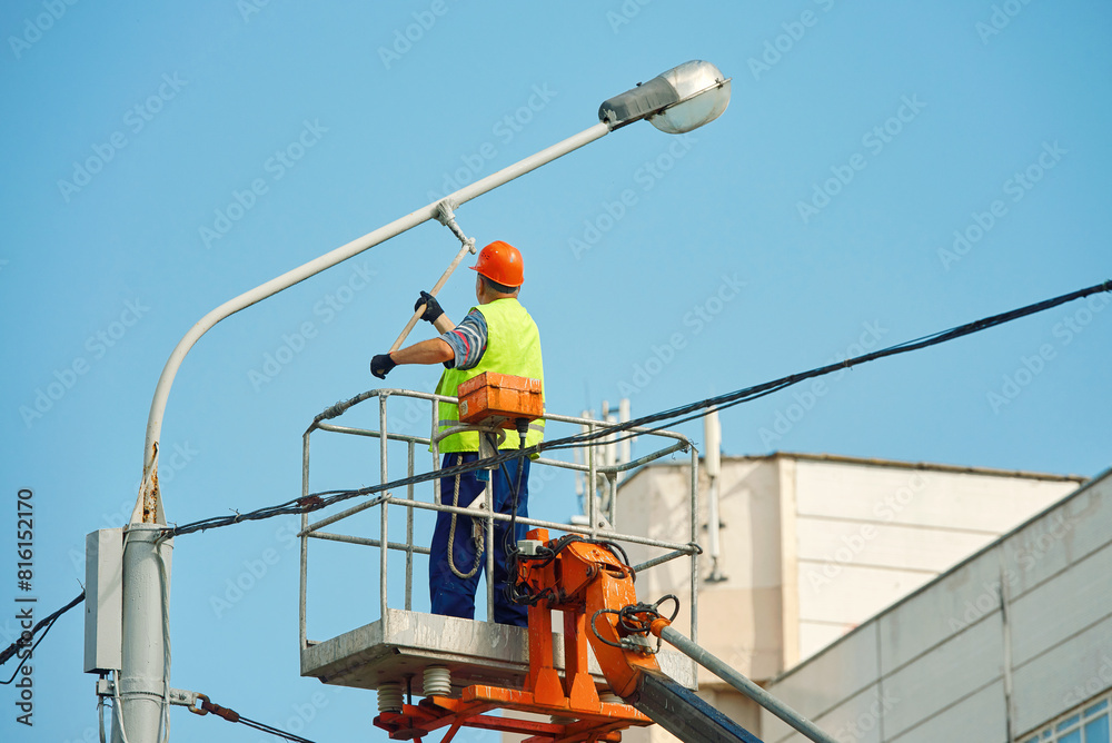 Utility worker paint street light pole, painting lamppost with brush. Painter in lift bucket