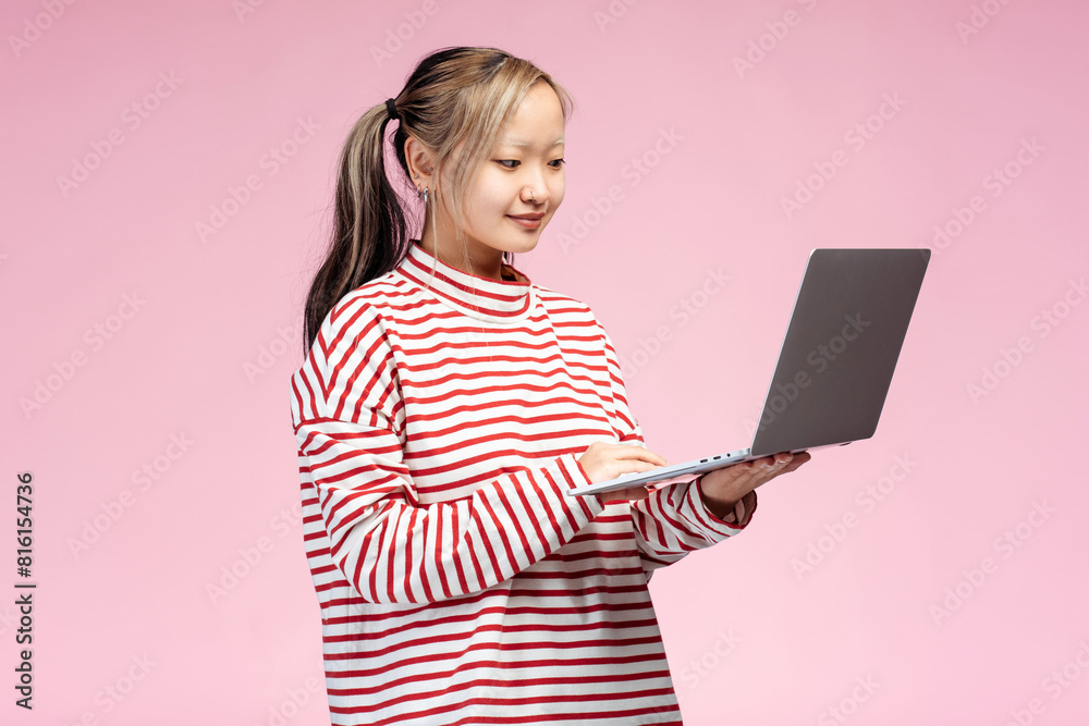 Happy cute Asian student using laptop looking at screen, isolated on pink background Happy cute Asian student using laptop looking at screen, isolated on pink background