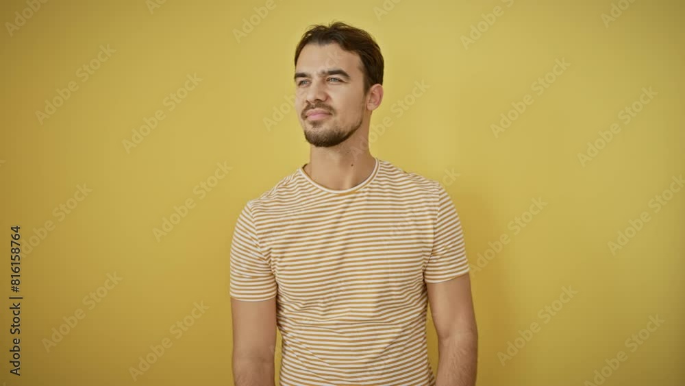 Young hispanic man wearing stripes t shirt standing looking away to side with smile on face, natural expression. laughing confident. over isolated yellow background Young hispanic man wearing stripes t shirt standing looking away to side with smile on face, natural expression. laughing confident. over isolated yellow background