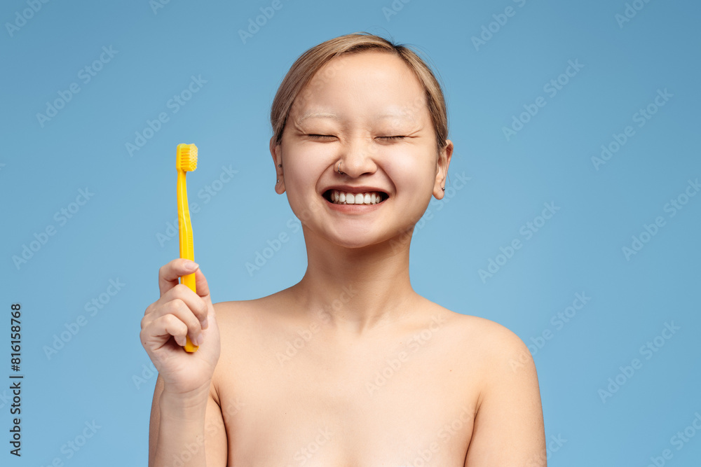 Happy Asian girl with closed eyes showing toothbrush isolated on blue background Happy Asian girl with closed eyes showing toothbrush isolated on blue background