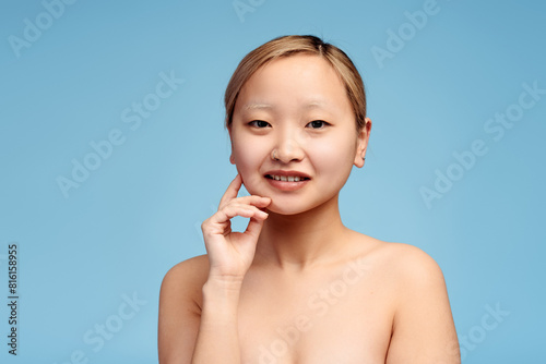 Pretty Asian girl holding hand on the cheek looking at camera, isolated. Spa concept