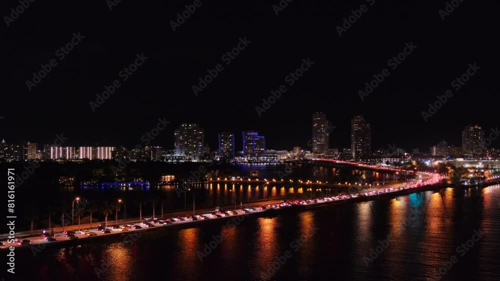 Distant night panoramic view from sea of Miami, Florida, USA, snaking road of MacArthur Causeway Bridge over dark water, lights of cars standing in traffic jam entering city. Downtown in background. Distant night panoramic view from sea of Miami, Florida, USA, snaking road of MacArthur Causeway Bridge over dark water, lights of cars standing in traffic jam entering city. Downtown in background.