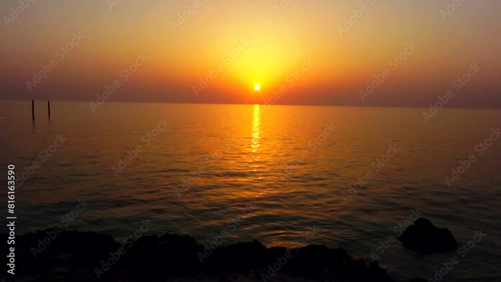 Long shot of a tranquil lake at sunset, with gentle waves creating a soothing rhythm on the water's surface, as the warm glow of the sun reflects off the water, casting a magical light.