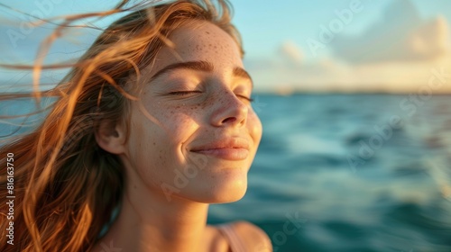 A woman is standing on the beach, feeling the wind in her hair and the warmth of the sun on her closed eyes. Her happy gesture reflects the joy of being in the moment AIG50