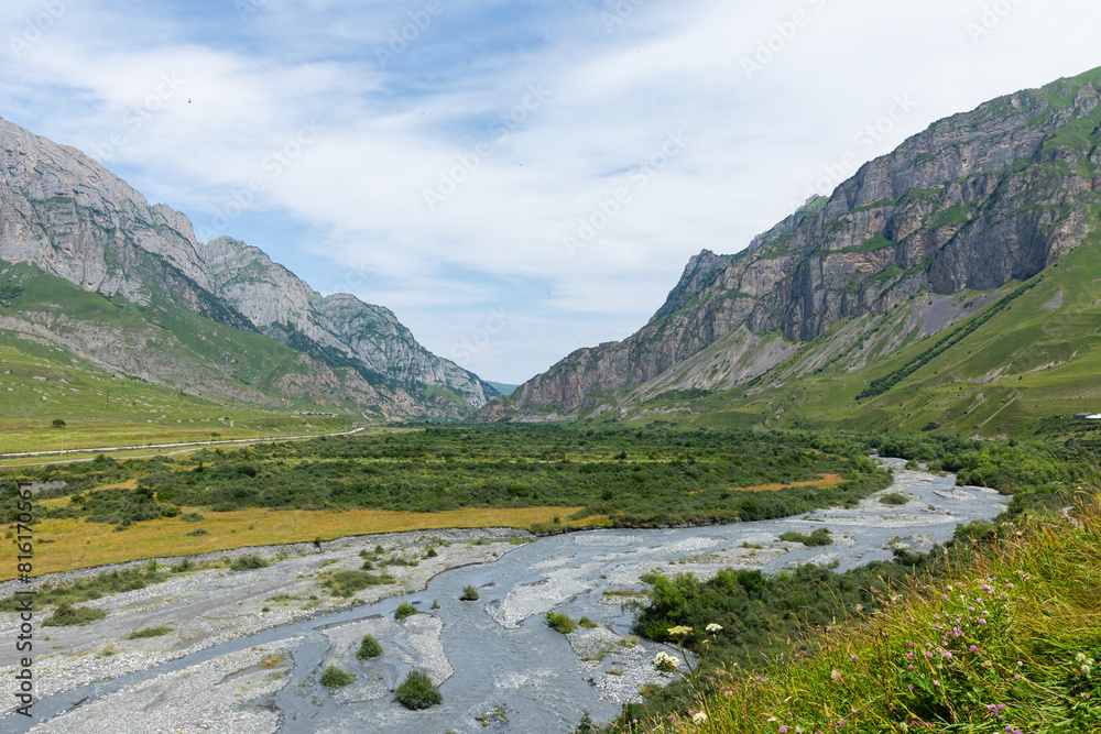 Mountain river of the village of Dargavs. Beautiful panorama of green alpine meadows, hills and mountains of North Ossetia, Russia. Mountain river of the village of Dargavs. Beautiful panorama of green alpine meadows, hills and mountains of North Ossetia, Russia.