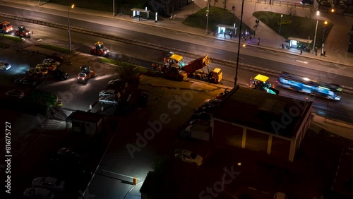 Time lapse of working road construction paving machines on the street of the night city, a team of road builders align the asphalt during moving cars and buses pass by