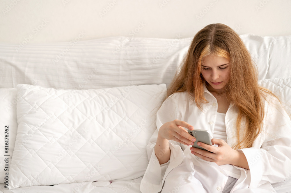 Bored lazy teenage girl with mobile phone sitting on bed, watching videos, scrolling social media chats, youth relax and leisure pastime, bad habits Bored lazy teenage girl with mobile phone sitting on bed, watching videos, scrolling social media chats, youth relax and leisure pastime, bad habits