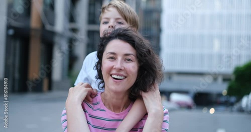 Portrait of adorable caucasian mother sitting and kid son hugging her from the back. Outdoor family day concept