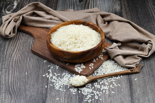 Raw white rice on wooden background. Long uncooked rice in wooden plate. Natural organic food. Traditional Asian cereal culture.