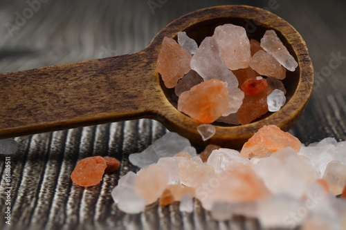 Pink Himalayan salt is poured with a wooden spoon. Himalaya salt on a dark background. Copy space. Macro Photography.