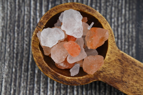 Pink Himalayan salt is poured with a wooden spoon. Himalaya salt on a dark background. Copy space. Macro Photography.