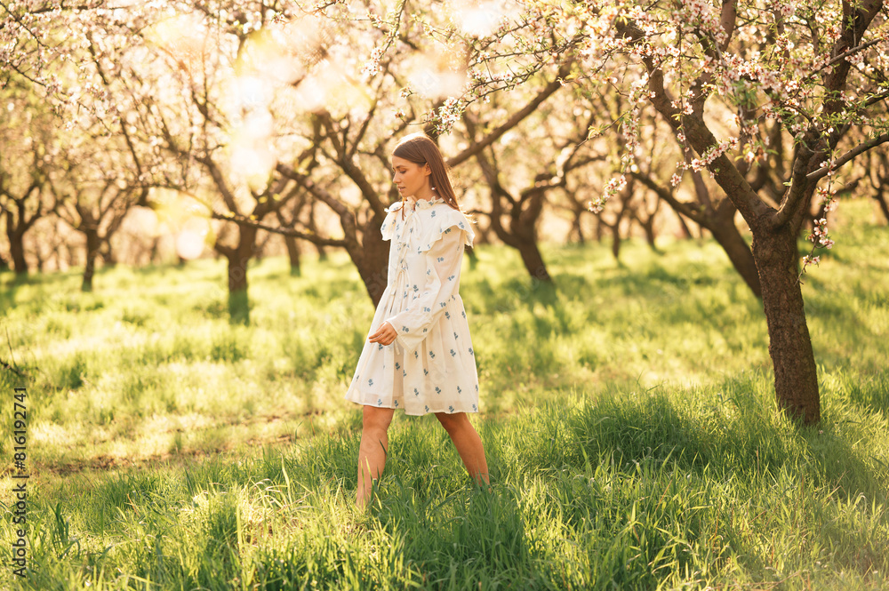 Young woman wearing white dress walking in almond orchard on a sunny day. Young woman wearing white dress walking in almond orchard on a sunny day.