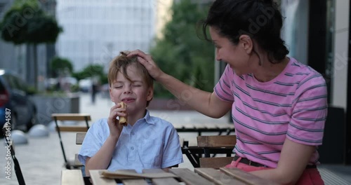 Young mother and her son having sweets in outdoor cafe on summer day. Sitting together, hugging and laughing, enjoying weekend or family day