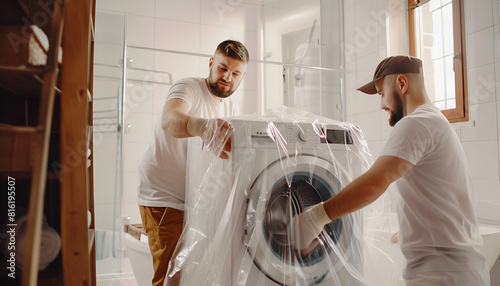 Male movers with stretch film wrapping washing machine in bathroom of new house photo