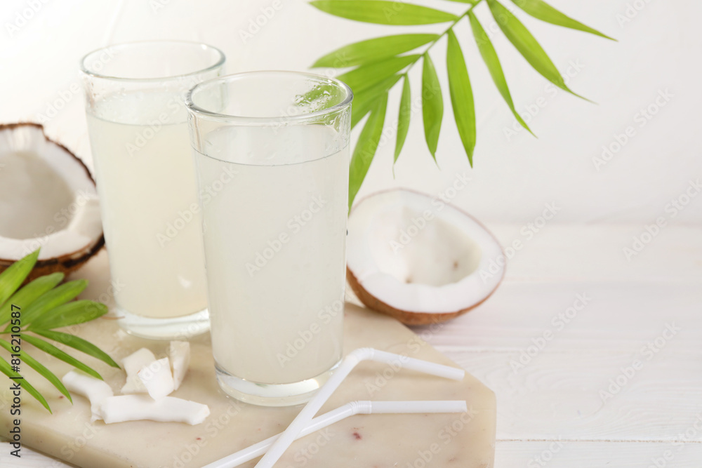 Glasses of coconut water, palm leaves and nuts on white table. Space for text Glasses of coconut water, palm leaves and nuts on white table. Space for text