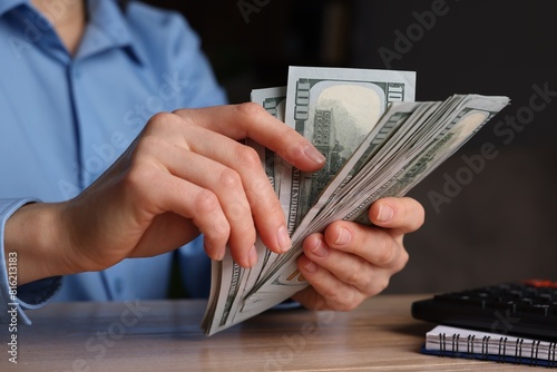 Money exchange. Woman counting dollar banknotes at wooden table, closeup