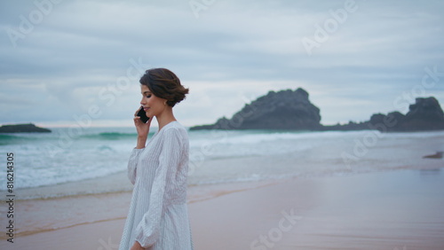 Smiling model calling cell on rocky tropical shore. Vacation girl going beach