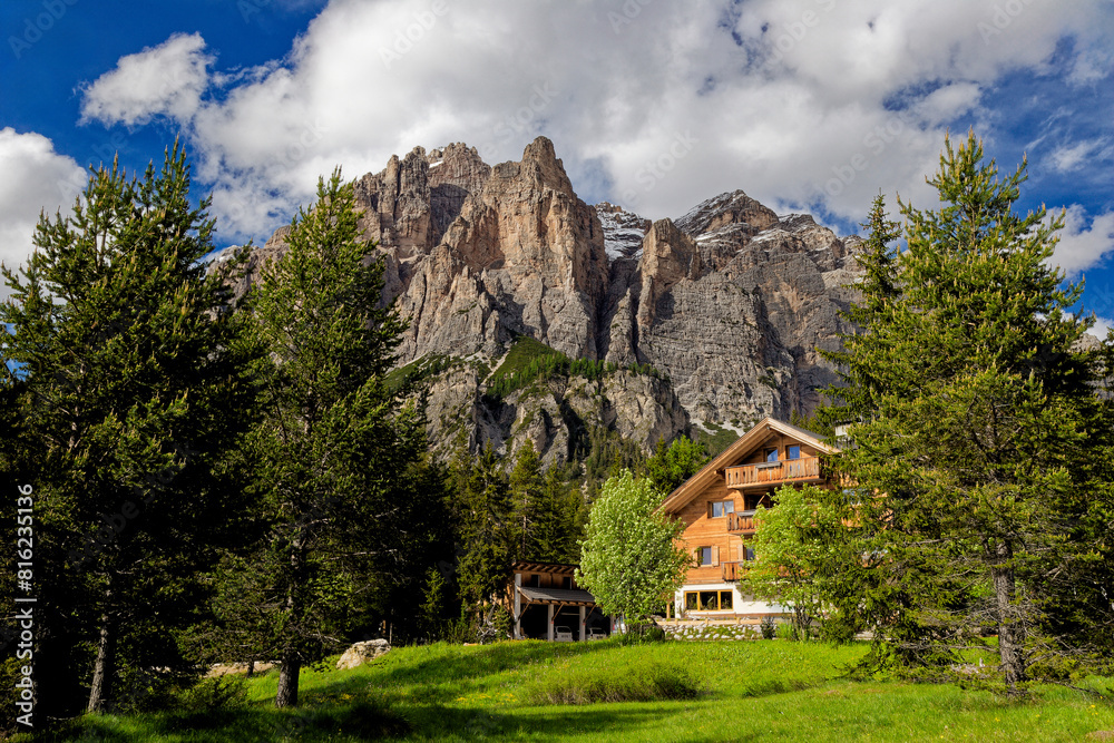 Alpine style house in the Italian Dolomite Mountains. Surrounded by pasture lands and rocky mountains. Alpine Landschaft. Idyllic mountain landscape in the Alps with meadows in summer.