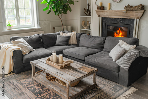 Grey cozy corner sofa and rustic coffee table in room with fireplace. French country farmhouse home interior design of modern living room. © Lucas