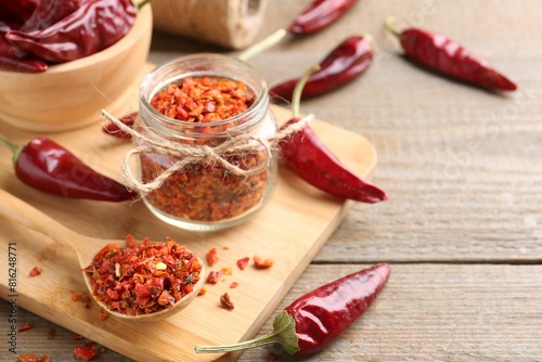 Chili pepper flakes and pods on wooden table, space for text