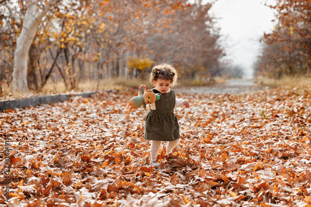 Child s autumn tale. Adorable little girl walking among golden autumn leaves with her teddy