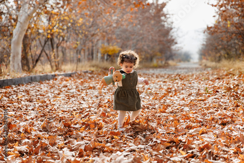 Obraz na płótnie Child s autumn tale. Adorable little girl walking among golden autumn leaves with her teddy w salonie