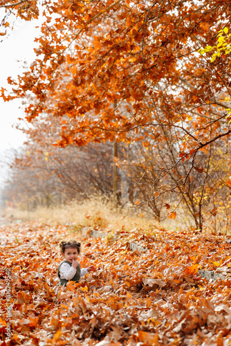 Obraz na płótnie Child's joy in autumn playing among colorful leaves on a serene fall day w salonie