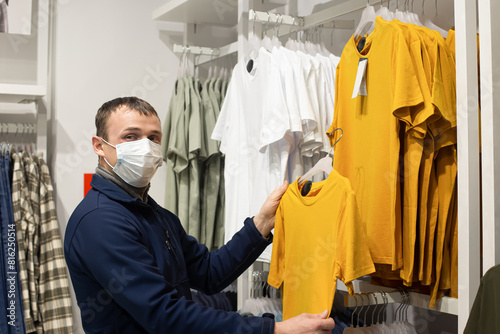 A man in a protective face mask chooses casual clothes. Clothing store. Retail trade