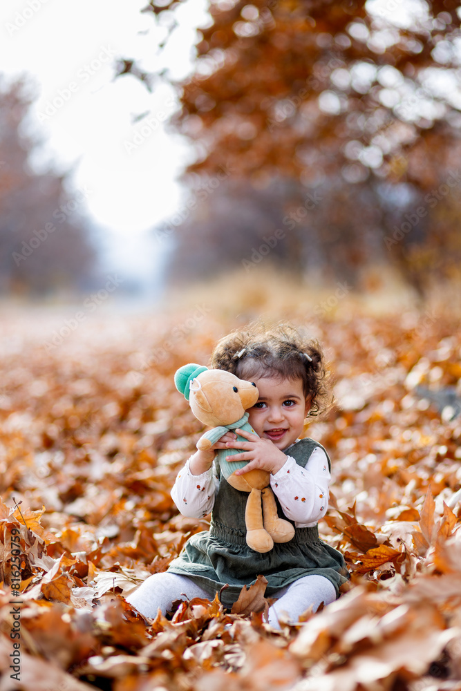 Lovely girl enjoying the day with her stuffed friend among the fallen leaves