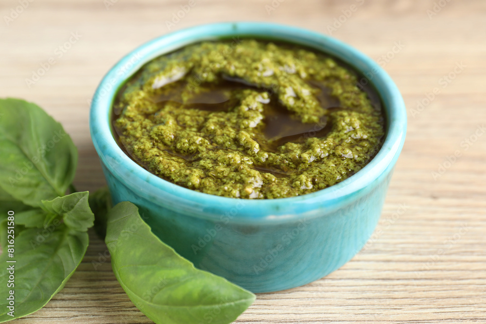 Tasty pesto sauce in bowl and basil on wooden table, closeup Tasty pesto sauce in bowl and basil on wooden table, closeup