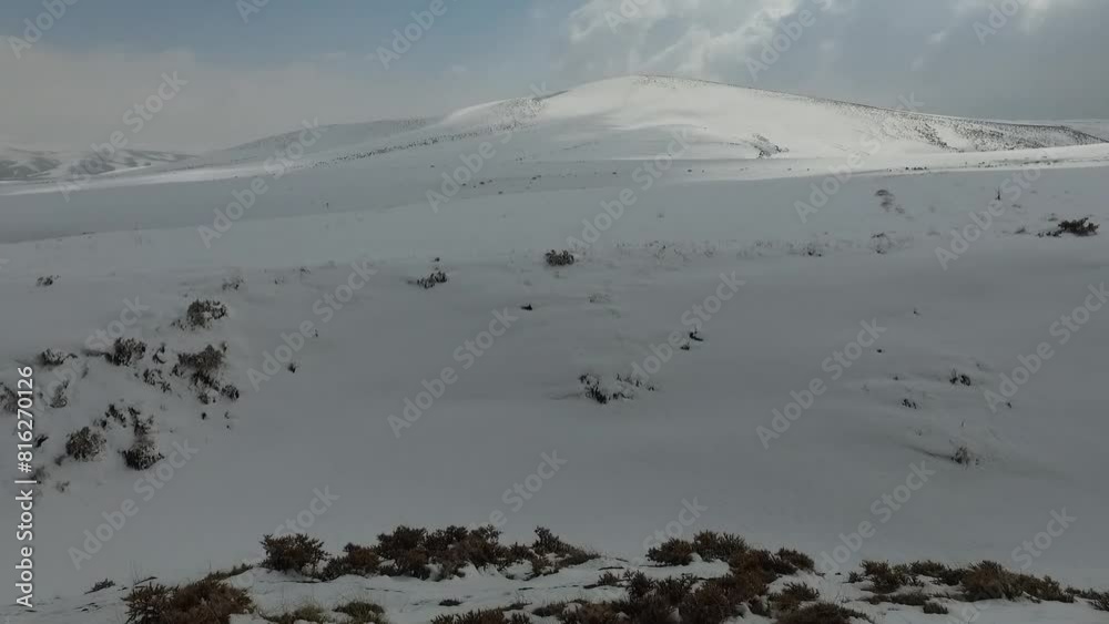 wide shot of a solitary snow covered hill rises up against a slowly shifting sky as fluffy white clouds drift overhead. wide shot of a solitary snow covered hill rises up against a slowly shifting sky as fluffy white clouds drift overhead.