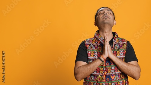 Pious indian man praying to his god, asking for forgiveness. Spiritual person doing worship hand gesturing, confessing, begging for pardon, isolated over studio background, camera A photo