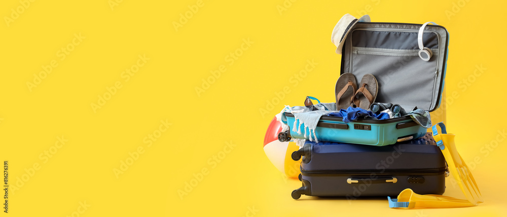 Fototapeta premium Suitcases with inflatable ball, beach accessories and headphones on yellow background. Summer vacation concept