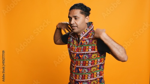 Excited person wearing traditional clothing having fun  dancing on oriental music. Delighted talented man doing entertaining bollywood dance moves  studio background  camera B
