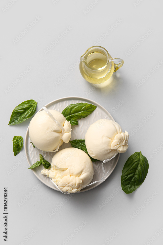 Plate of tasty Burrata cheese with basil and oil on white background Plate of tasty Burrata cheese with basil and oil on white background