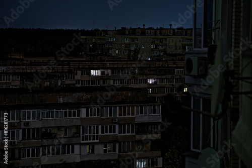 View on a panel residential buildings during blackout of electricity at night. Dark blue sky and forest on a background. Kyiv, Ukraine. Consequences after russian missile attacks.