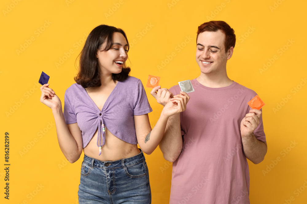 Young couple with condoms on yellow background. Safe sex concept Young couple with condoms on yellow background. Safe sex concept